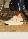 Detalle de costuras tono sobre tono en zapatilla urbana de cuero beige.